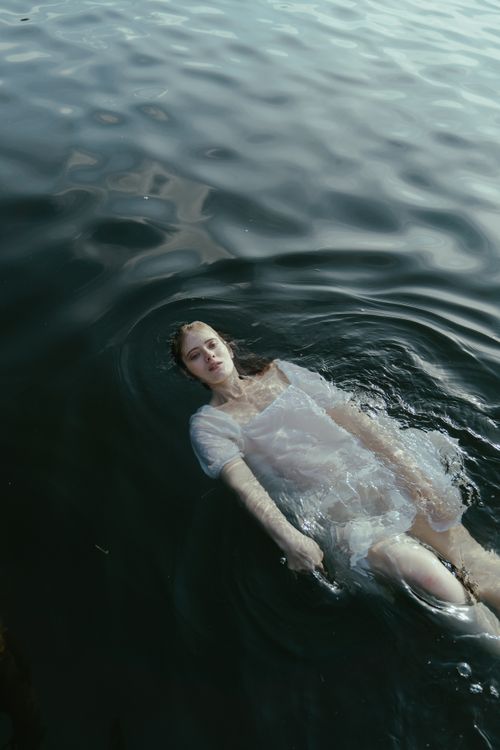 Free A woman in a white dress floats peacefully in dark water, evoking tranquility. Stock Photo