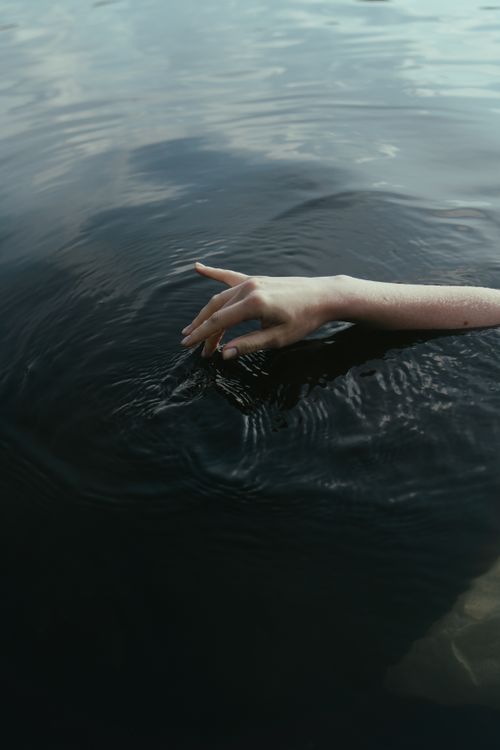 Free A close-up of a hand gently touching a calm water surface, creating ripples. Stock Photo