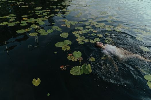 一名女子平静地漂浮在睡莲环绕的湖中，呈现出一片宁静的景象