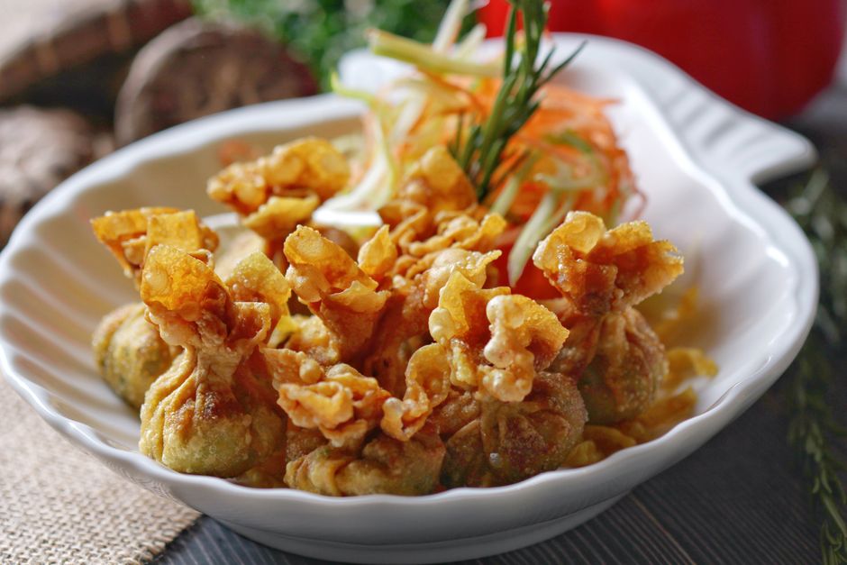 A pile of golden, blistered fried wonton wrappers stacked on a white plate with a small bowl of sweet chili dipping sauce beside them.