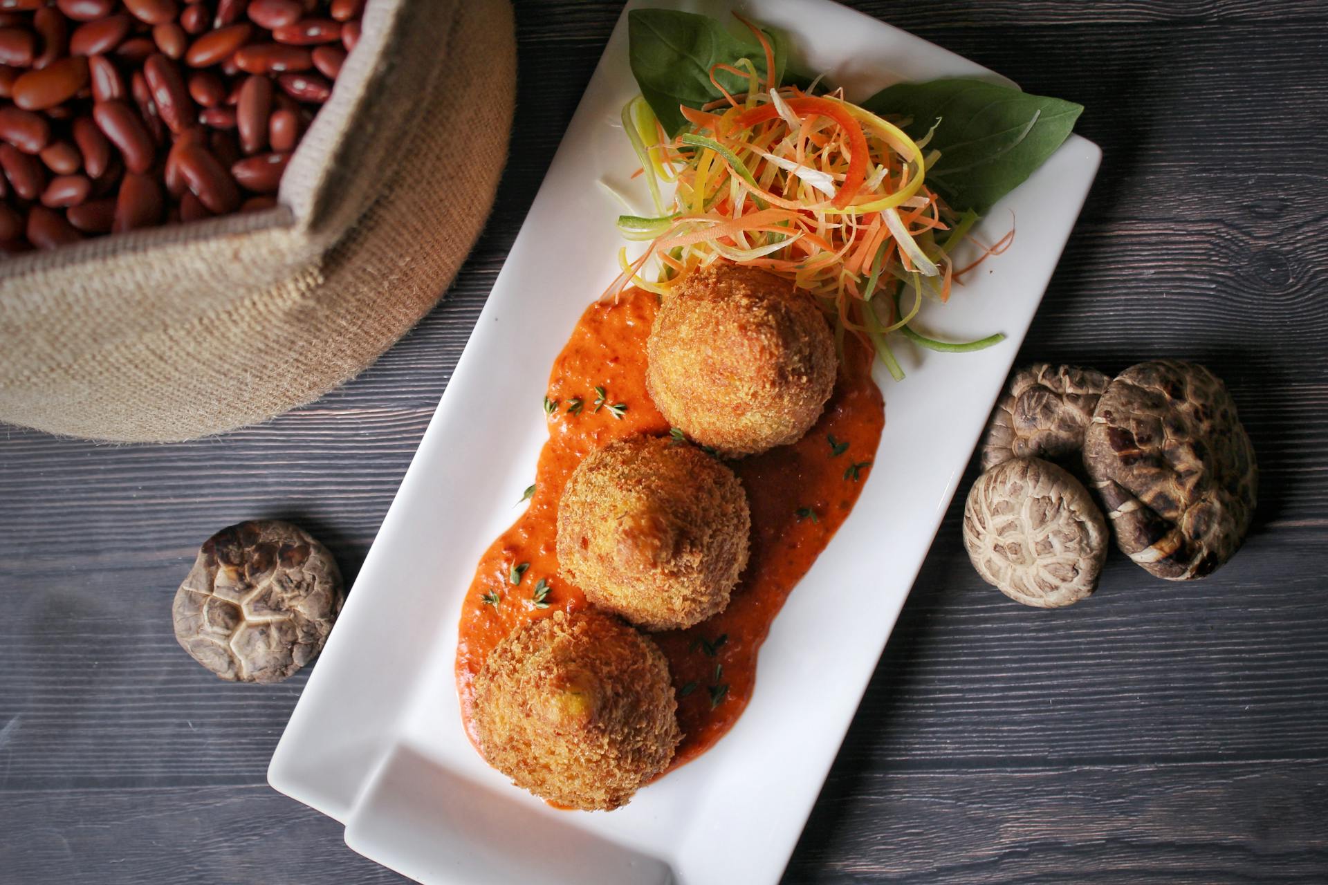 Delicious croquettes served on a white plate with red sauce and fresh vegetables.