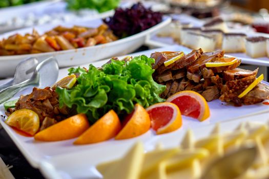A vibrant buffet spread featuring sliced meats, fresh greens, and juicy citrus fruits on a serving board.