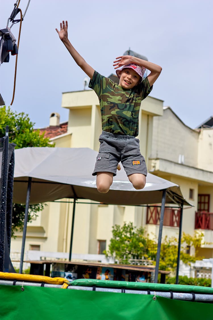 A Kid In Camouflage T-shirt Jumping On A Trampoline