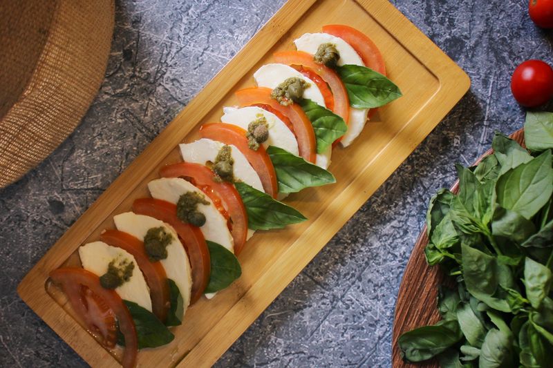 Sliced tomato, fresh mozzarella and basil laid out on a wooden board — photo by Shameel mukkath on Pexels