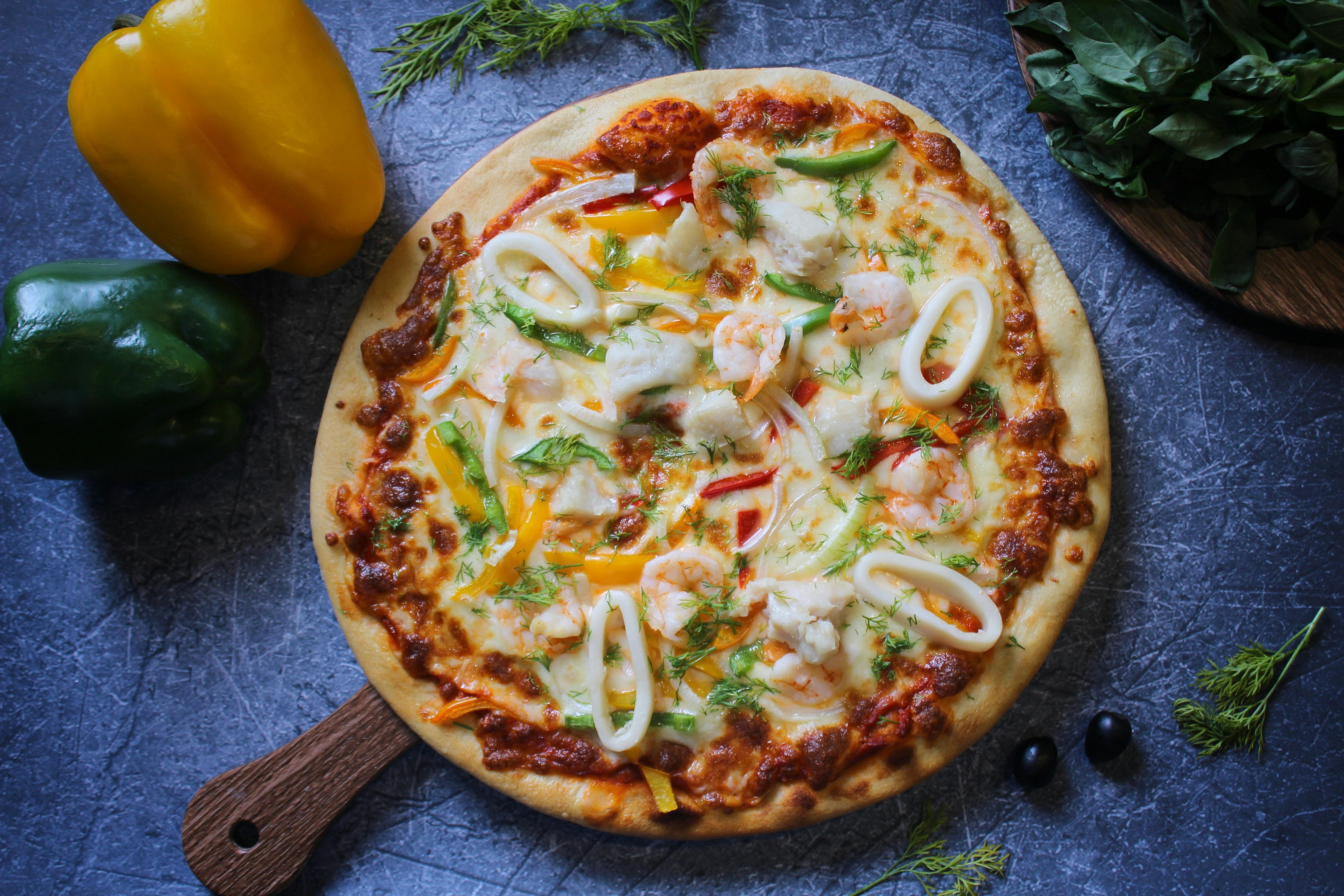 Delicious seafood pizza topped with shrimps, squid, and bell peppers on a wooden board.