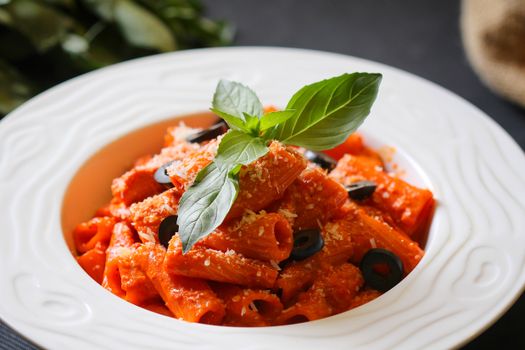 A plate of rigatoni pasta with tomato sauce, black olives, and fresh basil leaves.