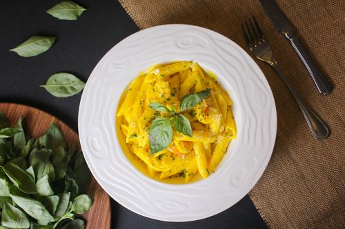Free Delicious penne pasta with creamy sauce and fresh basil garnish on a white plate. Stock Photo