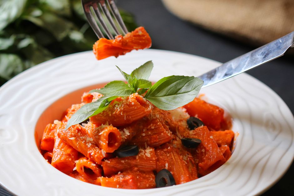 Tomato-based pasta sauce coating paccheri pasta with fresh basil garnish`