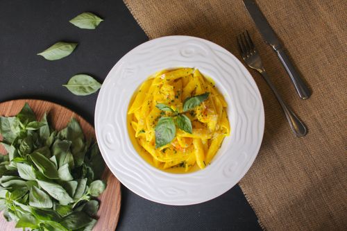 Free Top view of a plate of creamy penne pasta with fresh basil and cutlery on a rustic cloth. Stock Photo