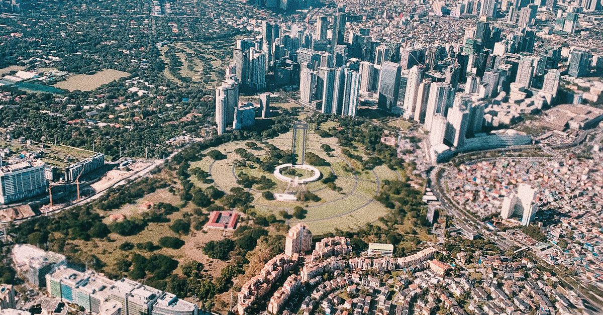 Aerial view from an airplane window overlooking a bustling city with skyscrapers, parks, and urban landscapes.