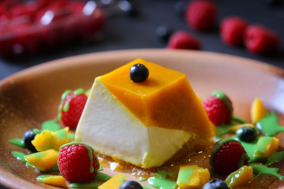 Pyramid-shaped panna cotta with mango layer, blueberry on top, raspberries, mango cubes and green sauce