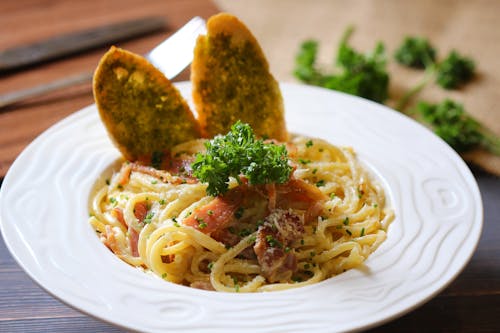 Pasta With Green Leaf and Brown Bread on White Ceramic Plate