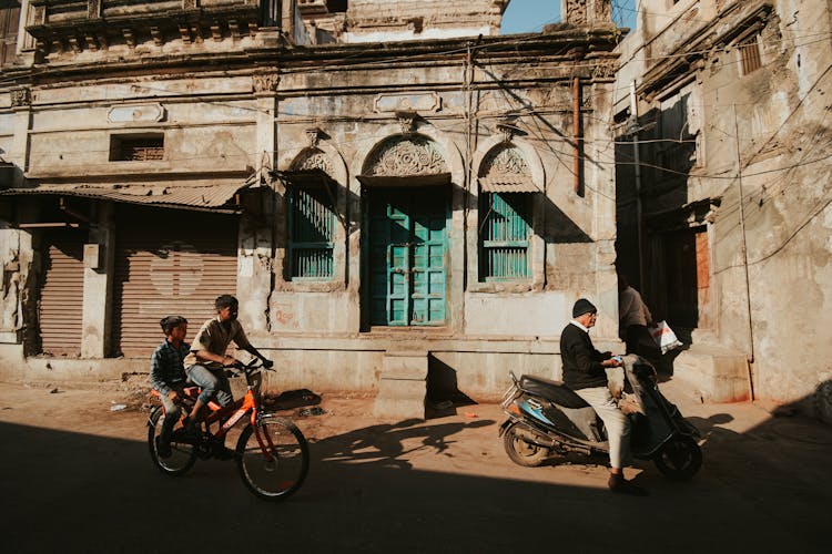 Kids On A Bicycle Near An Elderly Man Riding A Scooter