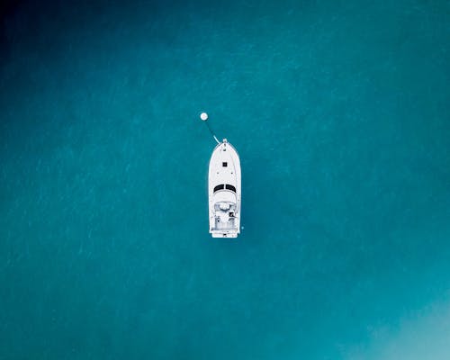 Drone view of modern white ship moored in still endless turquoise water of endless sea in nature in tropical country