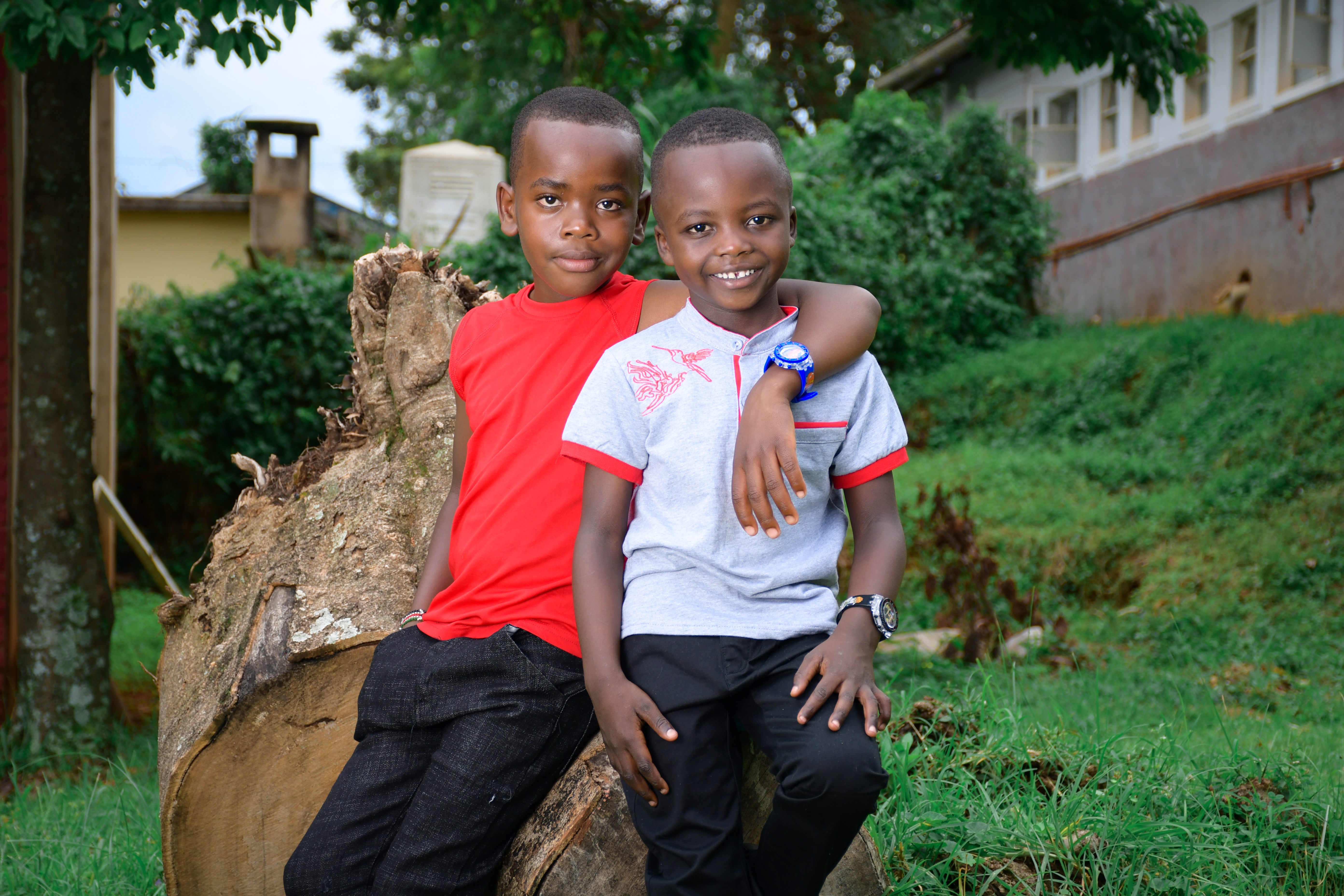 Two smiling boys sitting on a tree stump outdoors, embodying friendship and joy.
