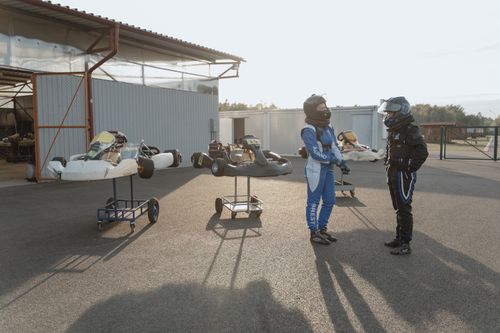 Free Two go-kart racers in protective gear standing trackside, preparing for a race outdoors. Stock Photo