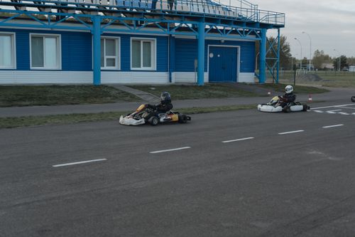 Free Two go-karts racing neck-to-neck on an outdoor track by a blue building. Stock Photo