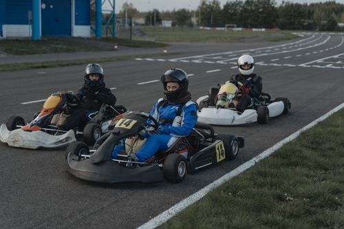 Free Three go-kart racers in protective gear sit ready on a racing track. Stock Photo