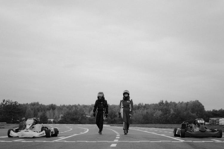 Monochrome Shot Of Two Go-Kart Drivers Walking In Racetrack