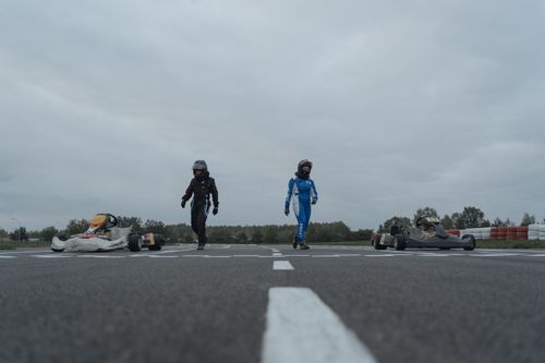 Free Two go-kart racers on a track in full gear, showcasing a motorsport moment. Stock Photo