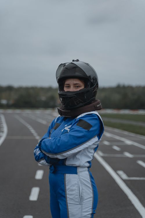 Free Racer in blue racing suit and helmet standing confidently on a race track. Stock Photo