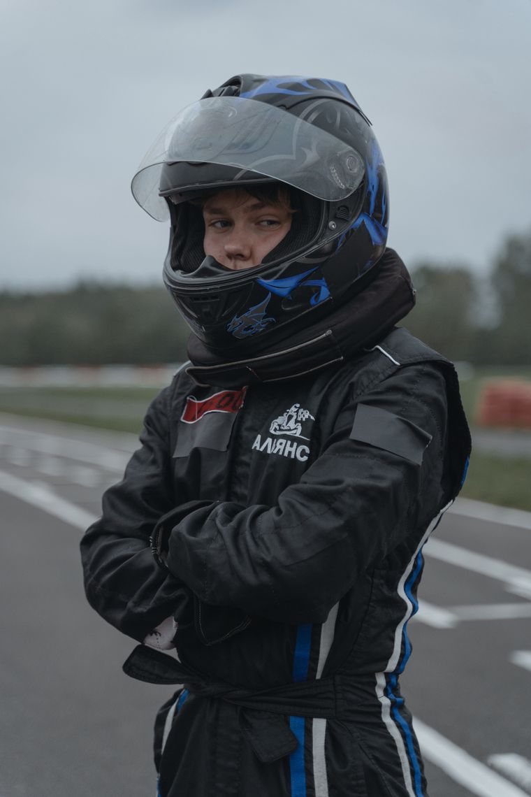 Young driver in full race gear beside an outdoor circuit — photo by Tima Miroshnichenko on Pexels