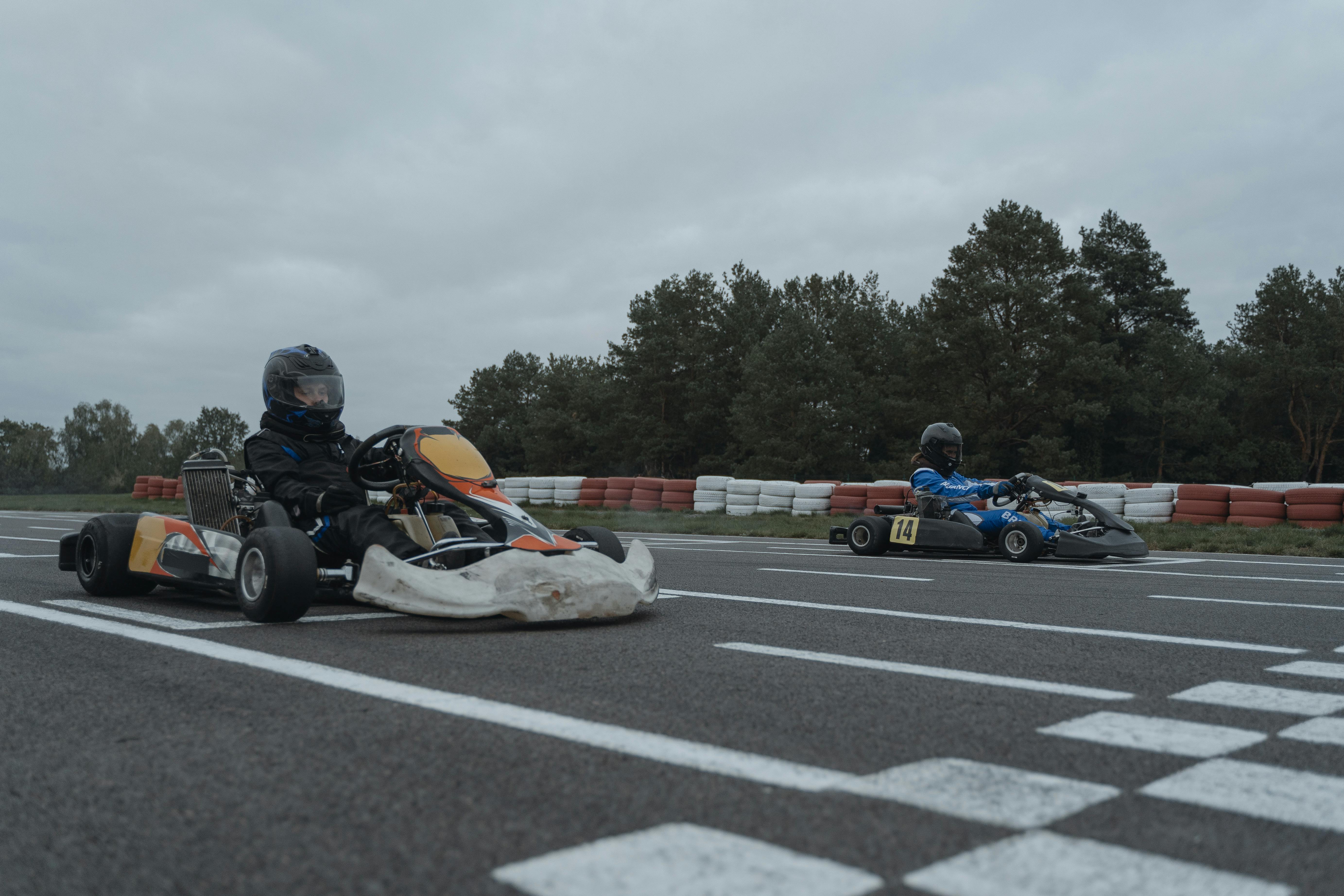 Two go-kart drivers at starting line of outdoor racetrack ready to race.