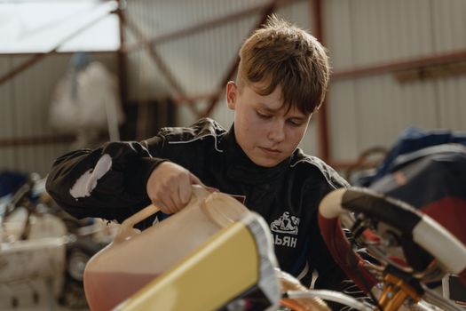 A young boy refuels a racing kart indoors, preparing for competition.