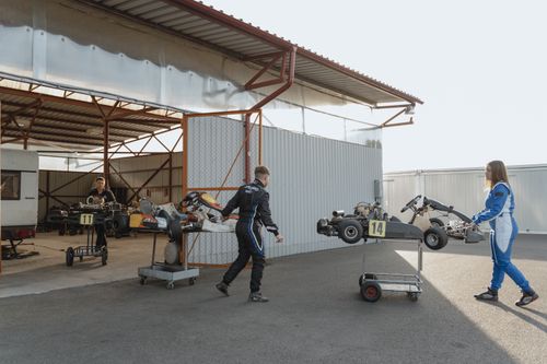 Free Teenagers in racing suits preparing go-karts for a race in a garage setting. Stock Photo