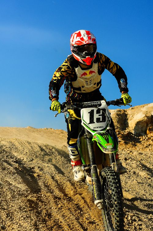 Free Motocross rider speeding on a dirt track under a clear blue sky, showcasing speed and skill. Stock Photo