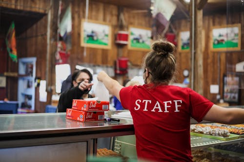 Free Back view of woman in staff t shirt giving order to female customer both wearing medical masks in cafe Stock Photo