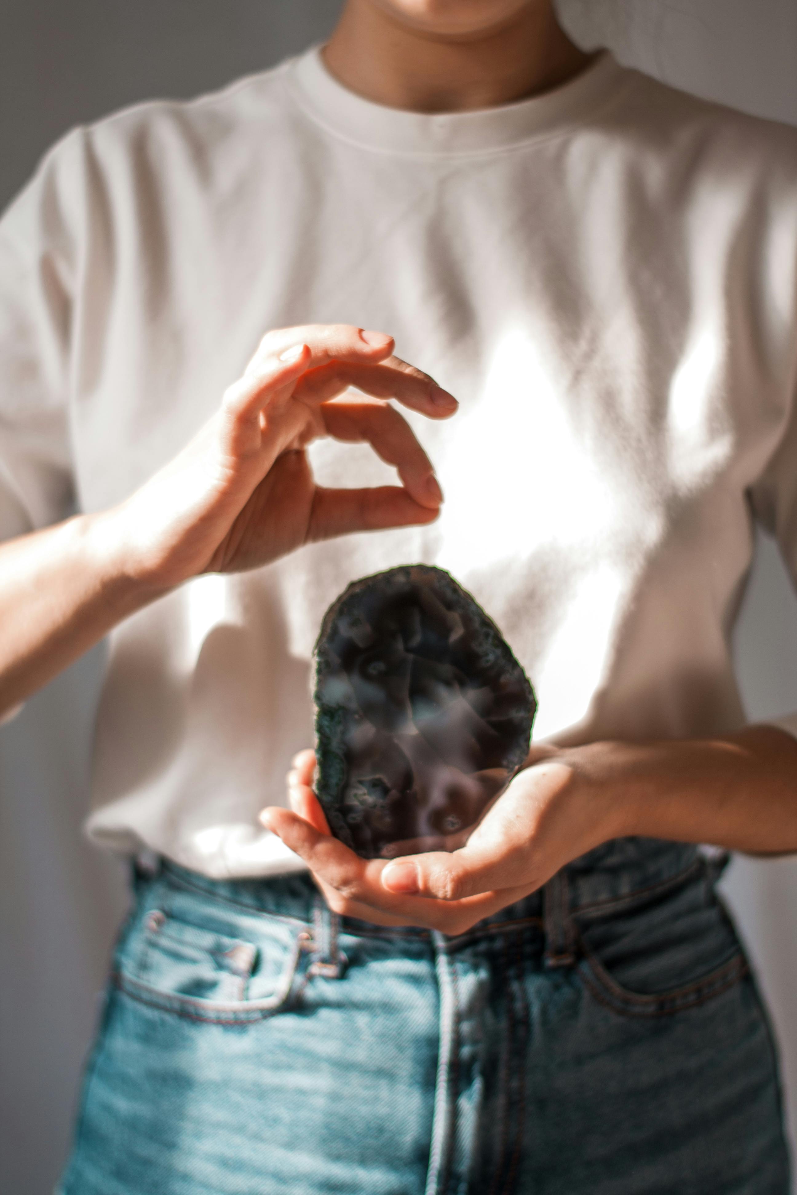 Free Crop faceless female in casual clothes standing against gray background and holding cosmic stone while showing gesture Stock Photo