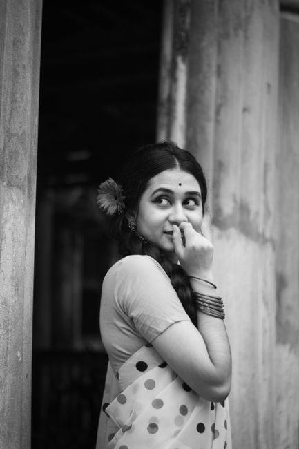 Black and white of cheerful ethnic female with bindi in sari looking away near shabby weathered wall of old house