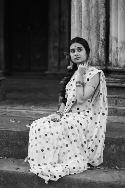 Free Black and white of charming young female wearing traditional sari sitting on stairs of old building and looking away Stock Photo