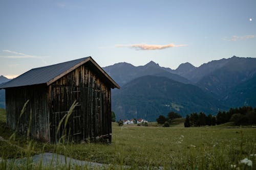 Old lumber hut in green valley with grass and high hills covered with forest