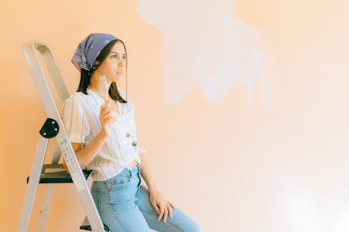 Woman Holding a Paintbrush Leaning on the Aluminum Ladder