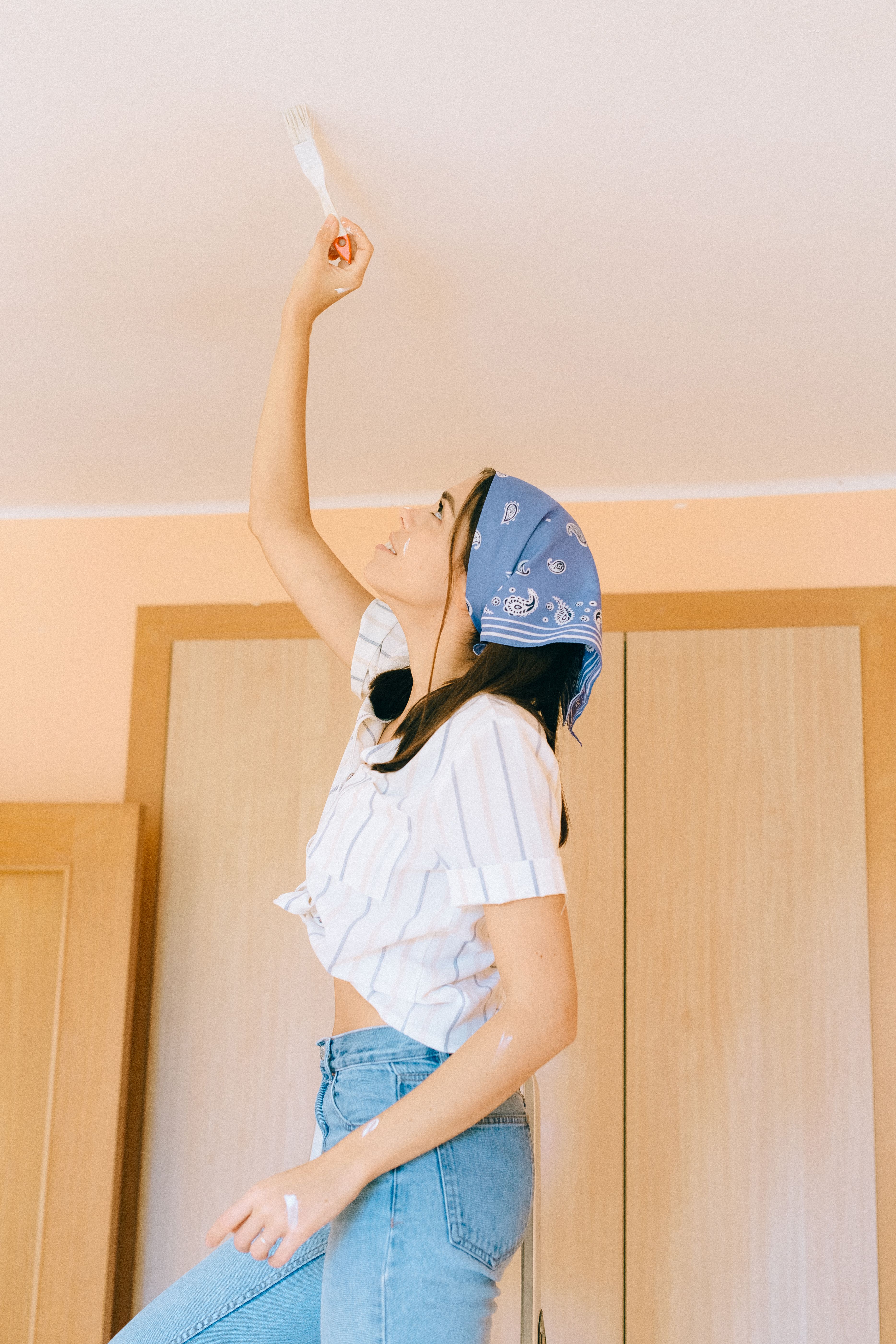 Painter rolling fresh paint onto a repaired ceiling inside a home