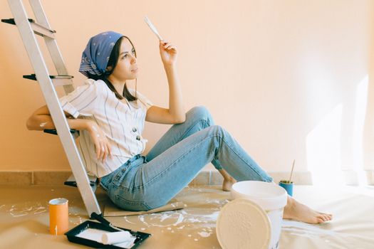 房间里，一名妇女赤脚坐在梯子上，手里拿着画笔