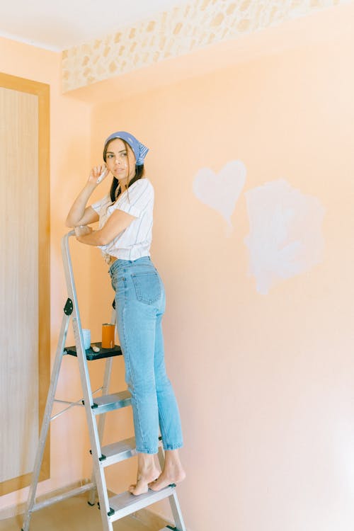 Woman in Striped Shirt and Denim Jeans Standing on a Ladder