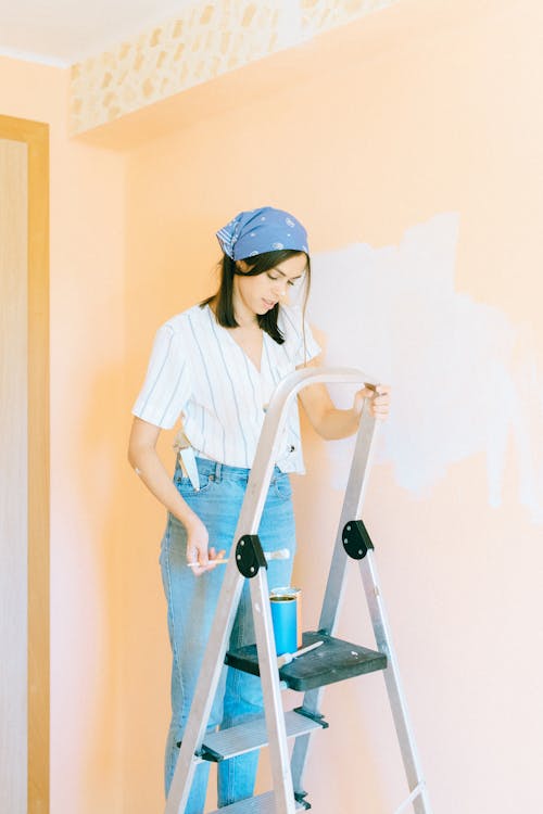 Woman Standing on Ladder While Holding a Paintbrush