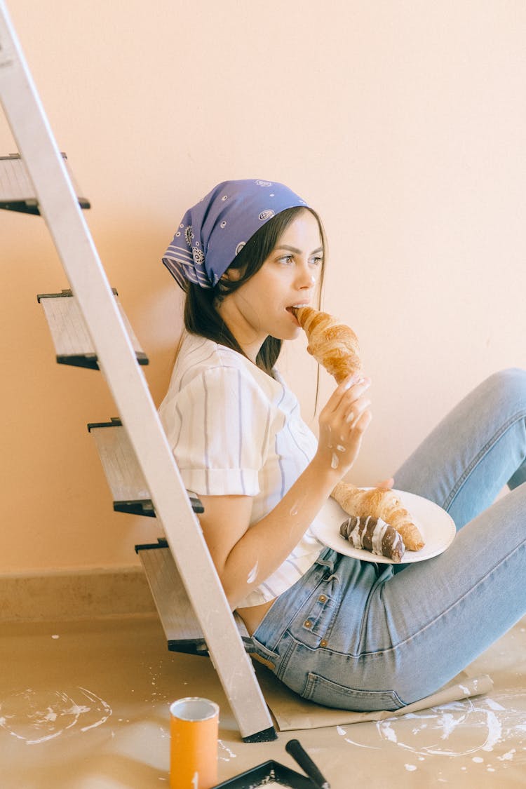 Woman Sitting On The Floor While Eating Croissant