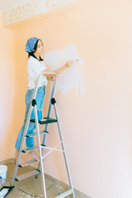 Person Standing on Stepladder While Painting Wall