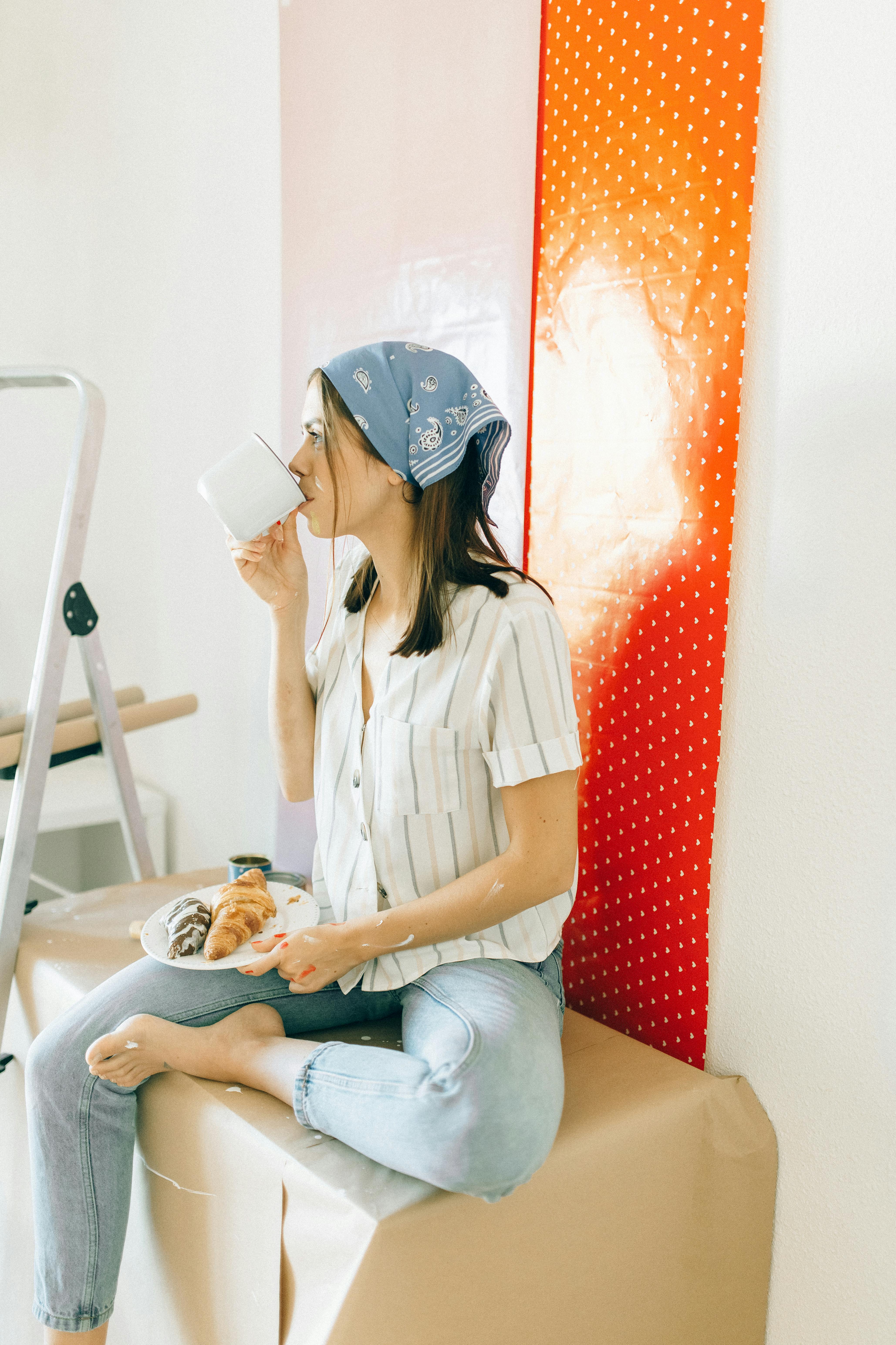 一名女子坐在室内桌旁，喝着咖啡，享用羊角面包