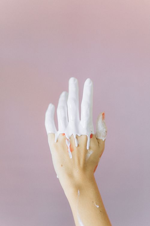 Free Close-up of a hand creatively drenched in white paint against a pastel pink backdrop, symbolizing creativity and abstract art. Stock Photo