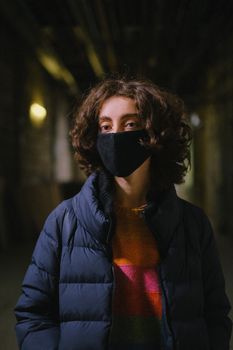 一个无脸的人穿着温暖的夹克和毛衣，戴着防护面具，站在黑暗的街道上看着相机