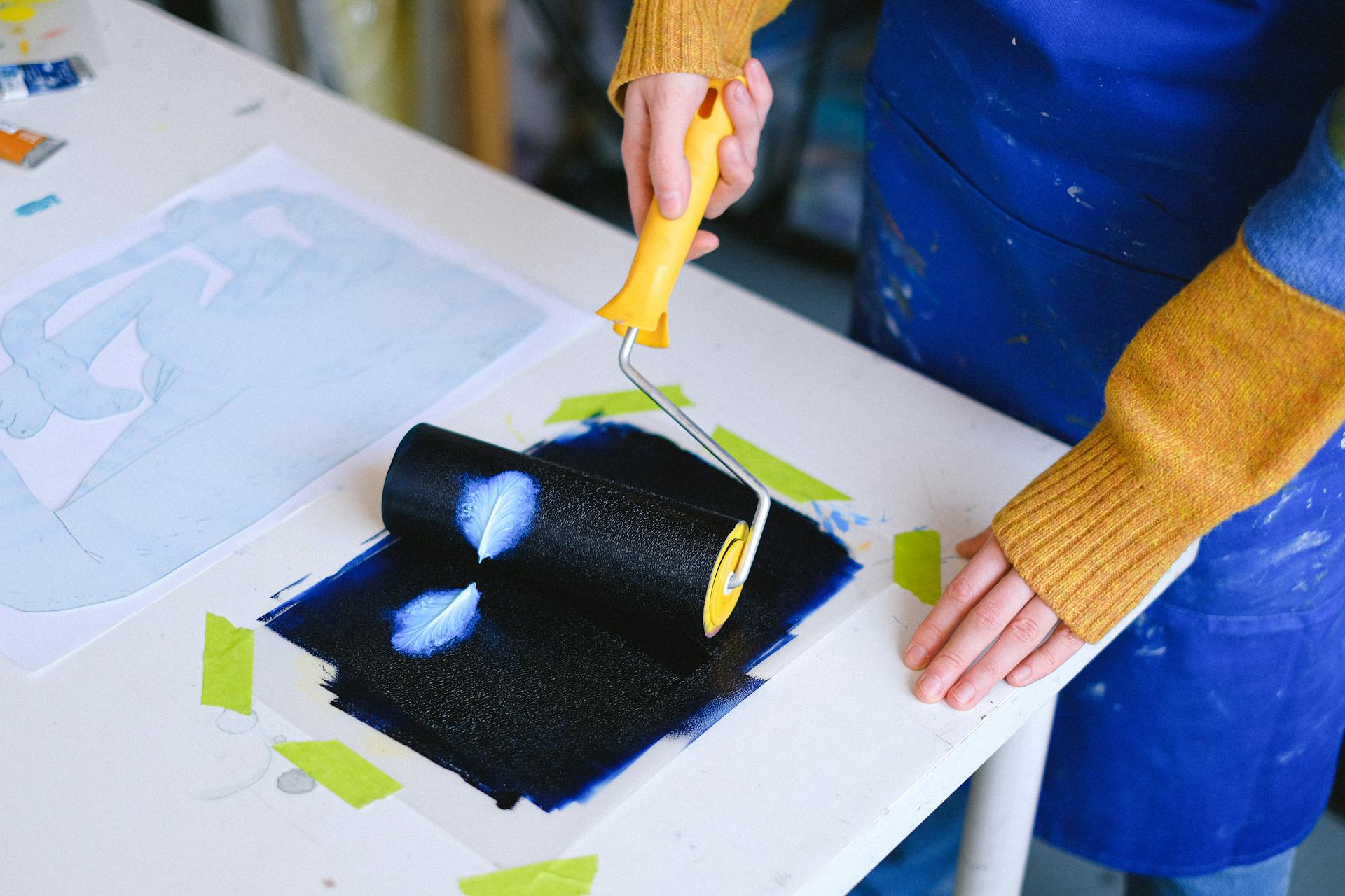 An artist in a workshop uses a paint roller on a table. Craft and creativity merge in this dynamic scene.
