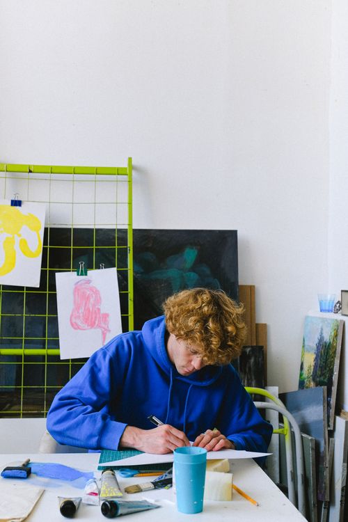 Free A young artist in blue hoodie creating artwork on a desk in a bright studio room. Stock Photo