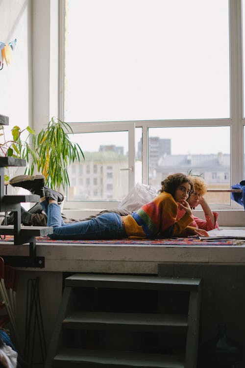 Side view of young designers lying on big windowsill and watching sketchbook in arts craft shop