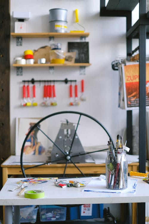 Interior of professional workplace of artist with desk with paint tubes printing press machine and hanging on wall tools