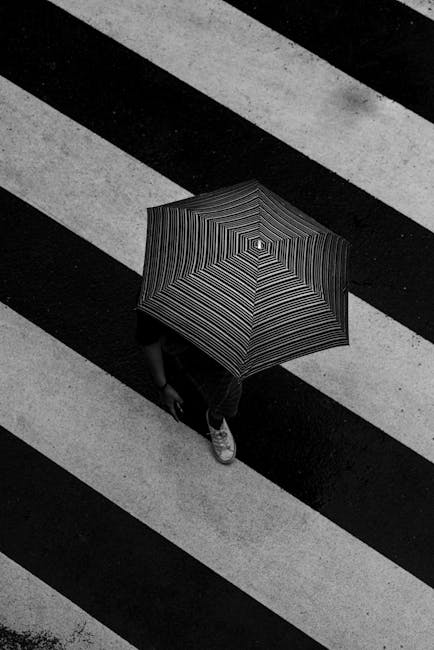 Black and white of faceless person under umbrella crossing street in rainy weather